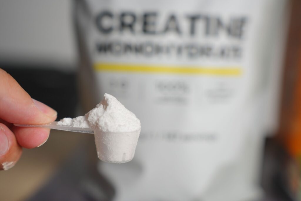 Close-up of hand holding measuring scoop filled with white creatine powder.